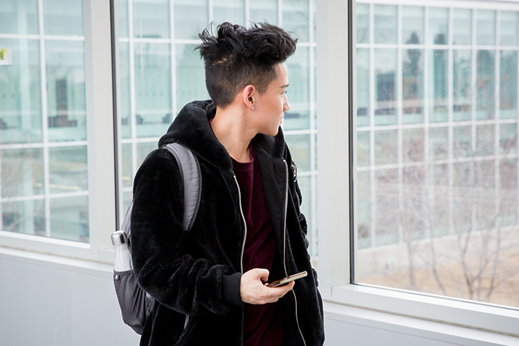 NAIT student walking in the hallway holding a cell phone.