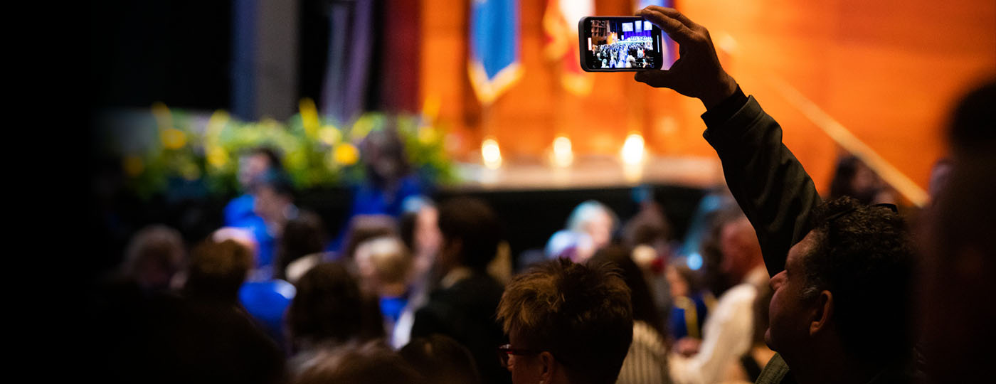 Family members watching the convocation ceremony, one holding a phone up to record the event.