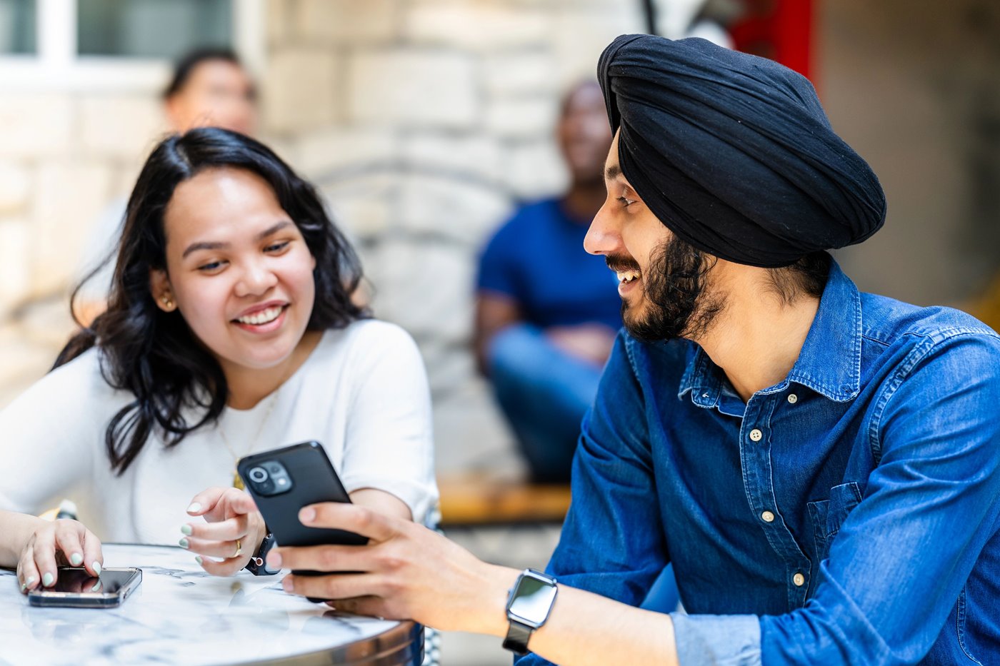 Two international students sit at a cafe table together and point to phone