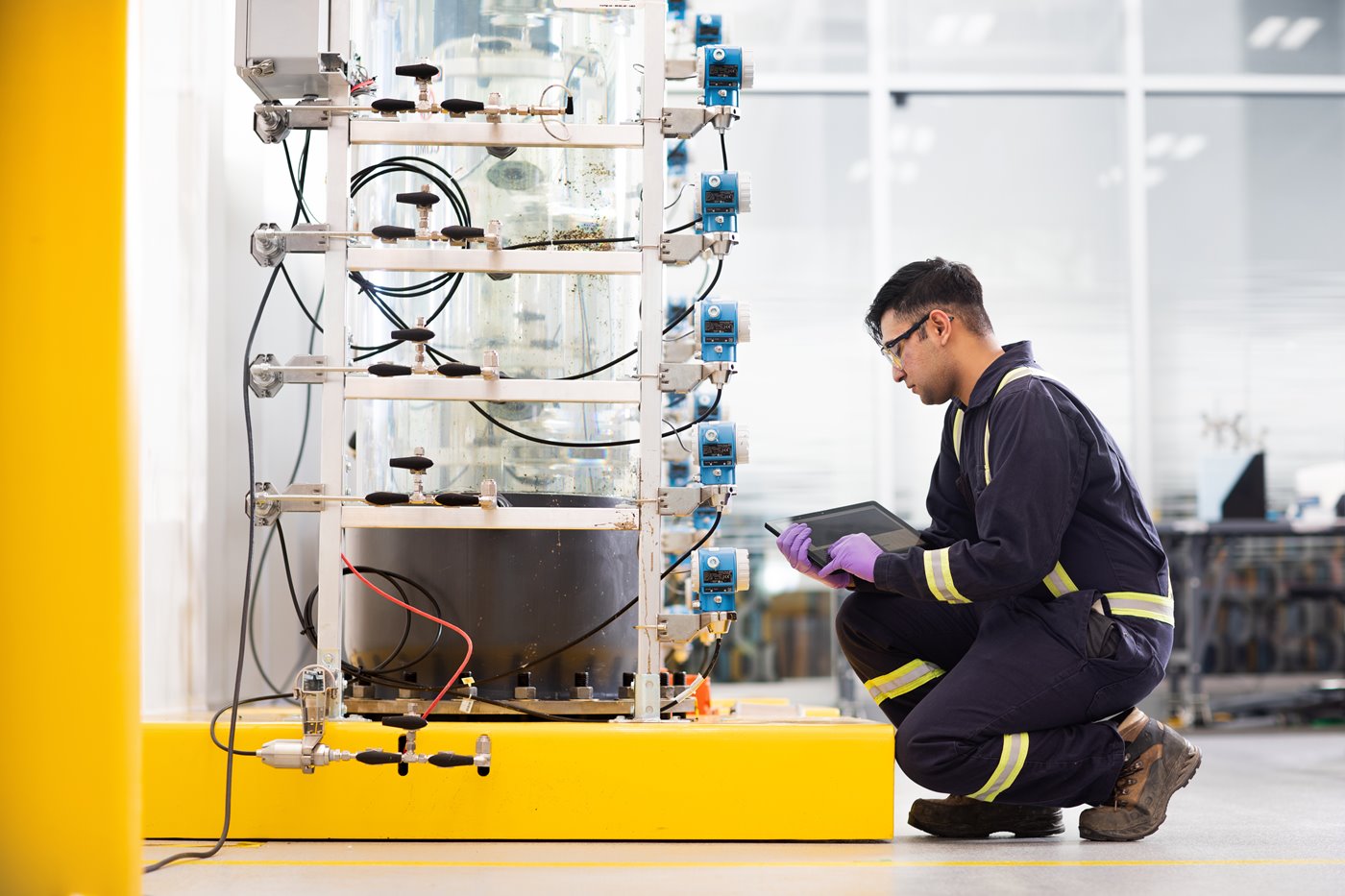 A scientist in safety equipment checking a sensor on a flocculation tube. 