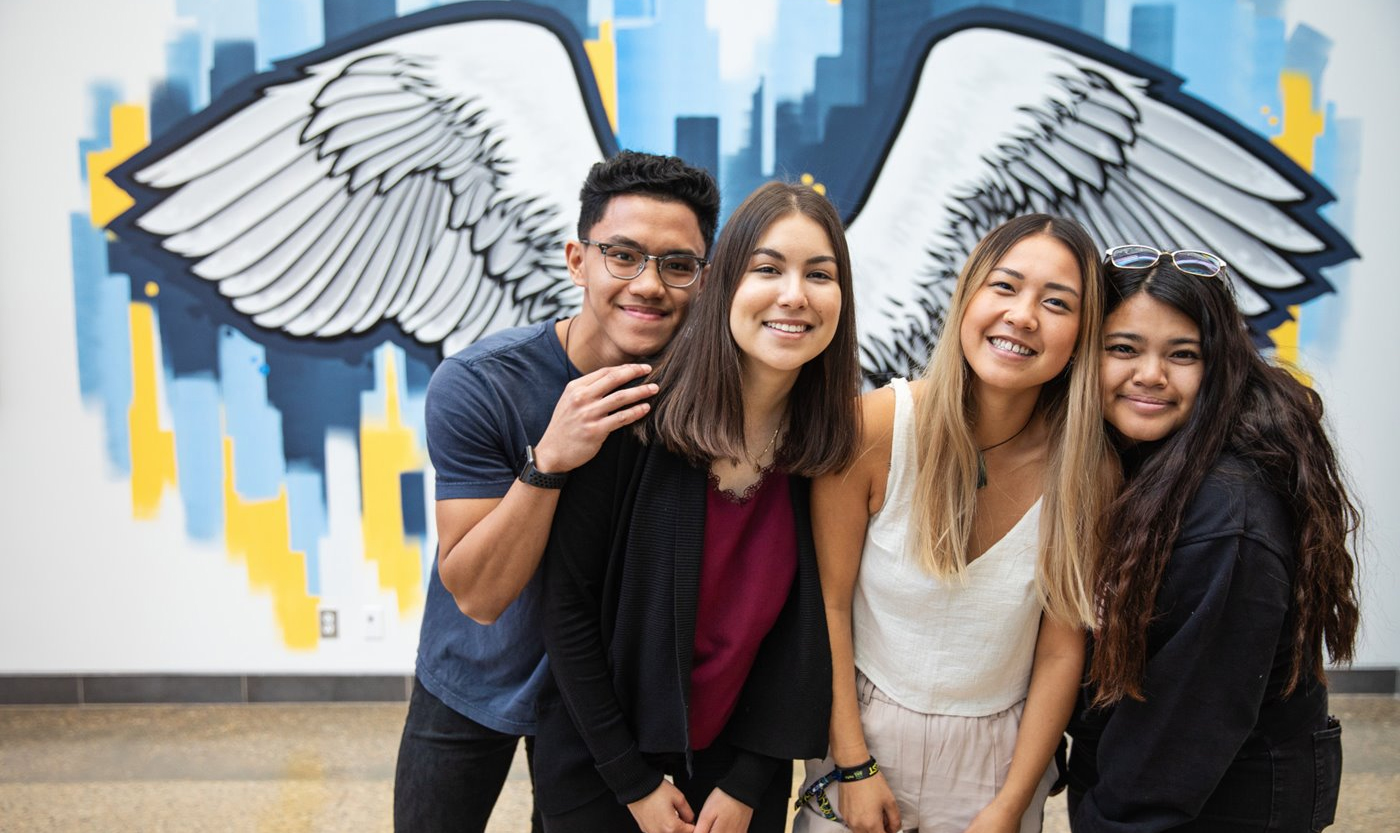 4 students smiling with art of angel wings in background