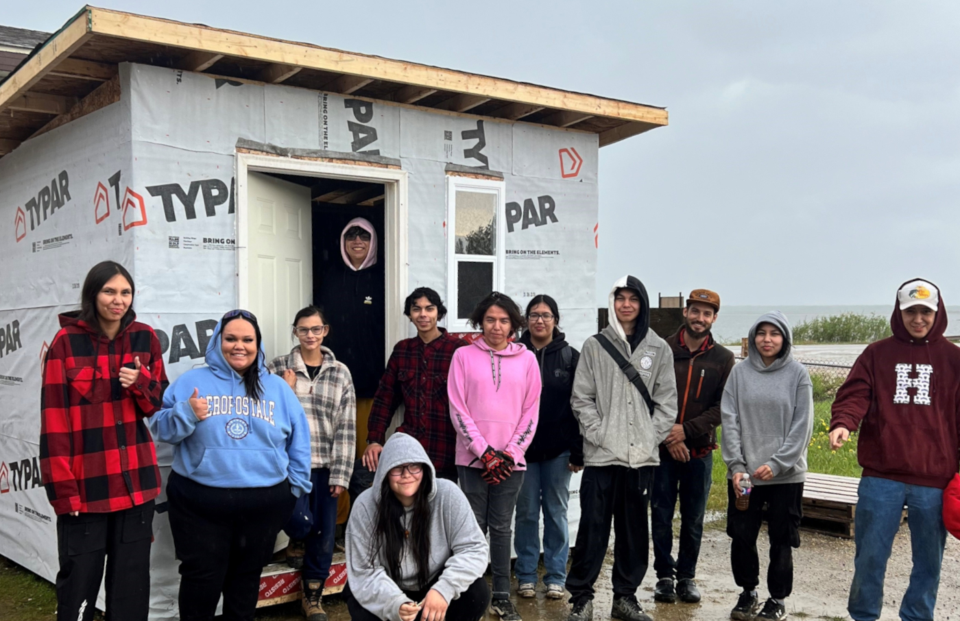 12 Indigenous students pose outside near a construction project they worked on