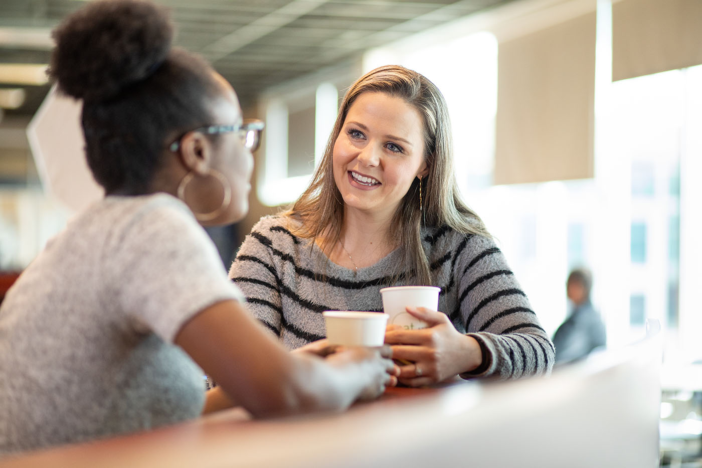 Two women with coffee cups having a conversation.