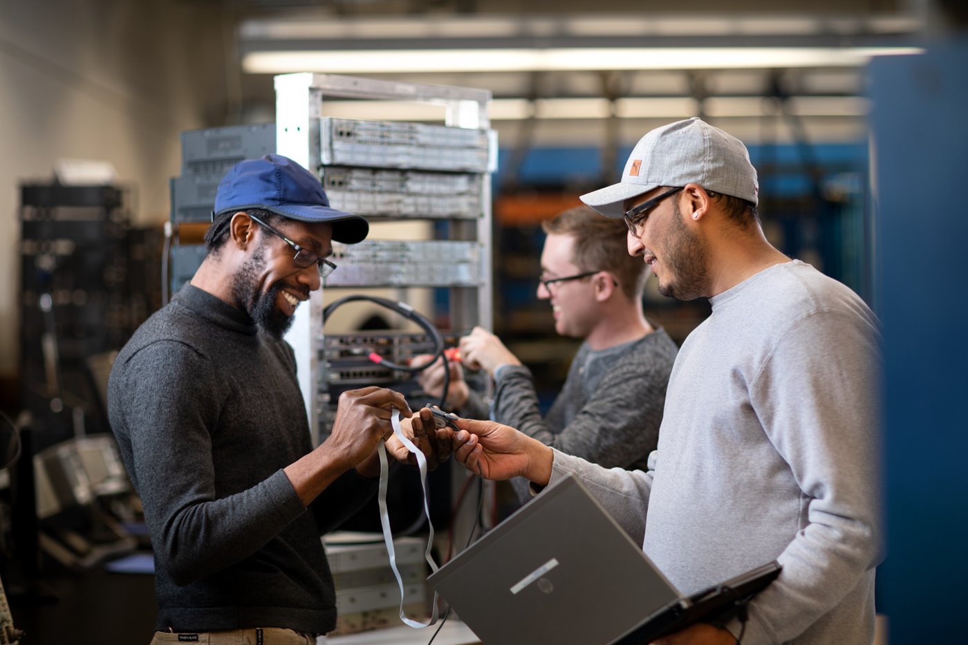 A group of men smiling while connecting a laptop to a server